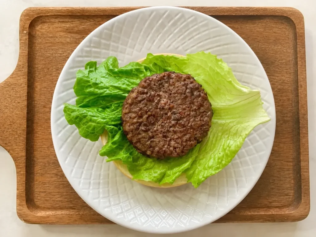 Cooked beef burger patty placed on lettuce and a burger bun